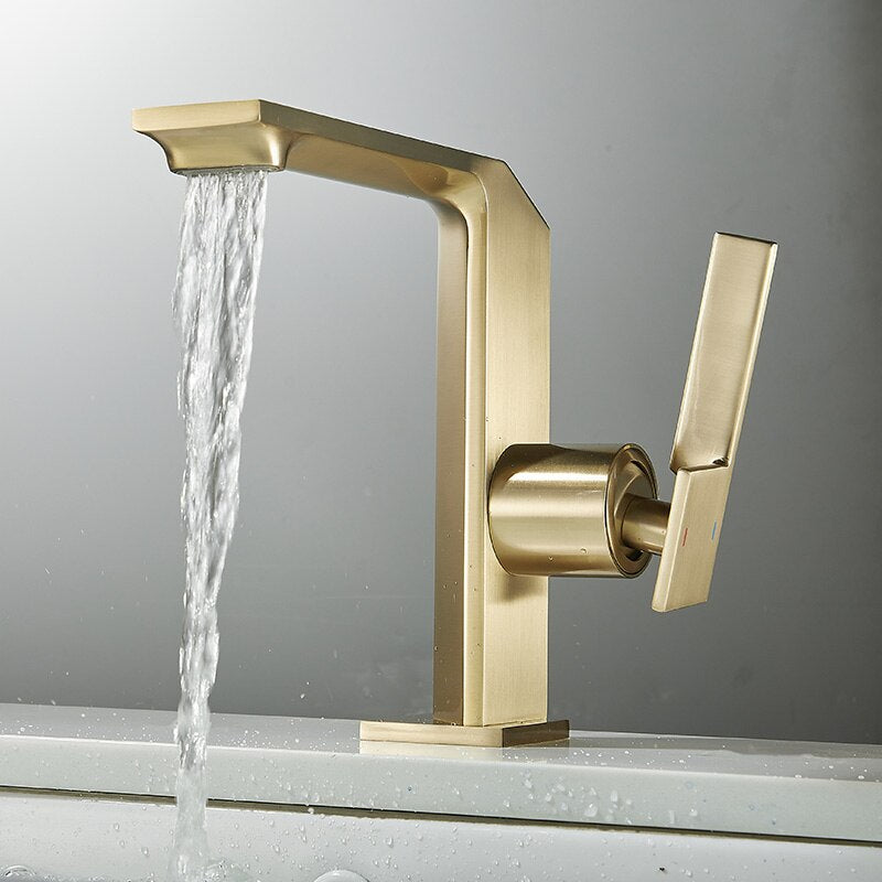 The Tiqui™ Solid Brass Bathroom Sink Faucet from Tiqui, featuring a modern matte gold finish and minimalist design, is pouring water into a white sink. It boasts a sleek, angular spout and an ergonomic single-lever handle, adding a touch of elegance to the bathroom with its sophisticated finish.