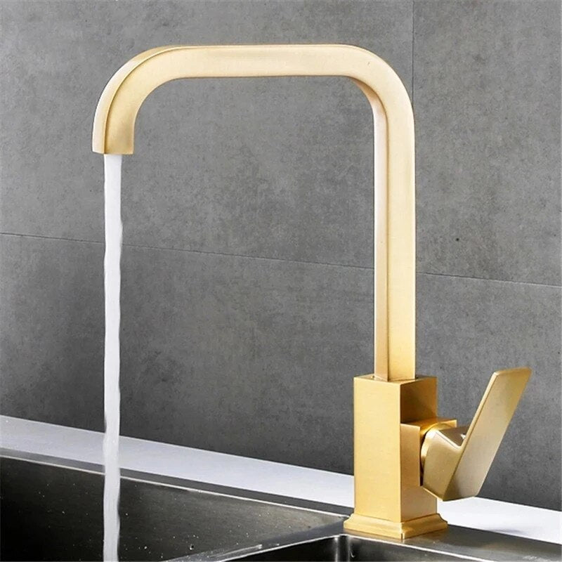 The Tiqui™ Solid Brass Single Handle Kitchen Faucet by Tiqui, featuring a sleek, modern golden finish and a square design, is shown mounted on a sink against a dark, tiled wall backdrop. Water is flowing from the faucet into the sink, and it has a lever handle on its side.