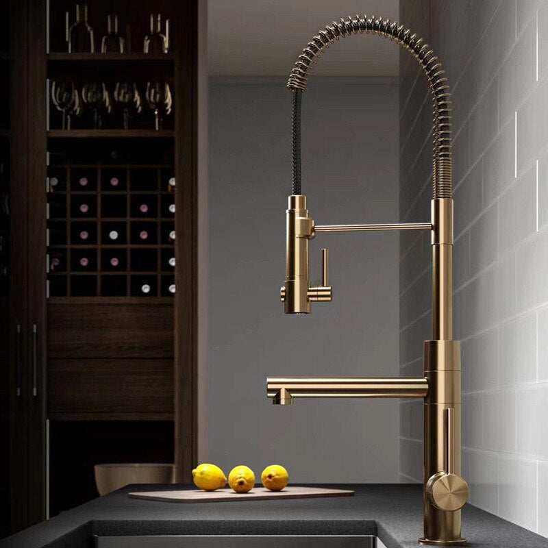 A modern kitchen sink with the stylish black and gold Tiqui™ Single Handle Pull Out Spout Kitchen Faucet by Smesiteli is seen. Water is flowing from the faucet into the sink. On the counter, there are white bowls, decorative items, a book titled "Company," and a potted plant.