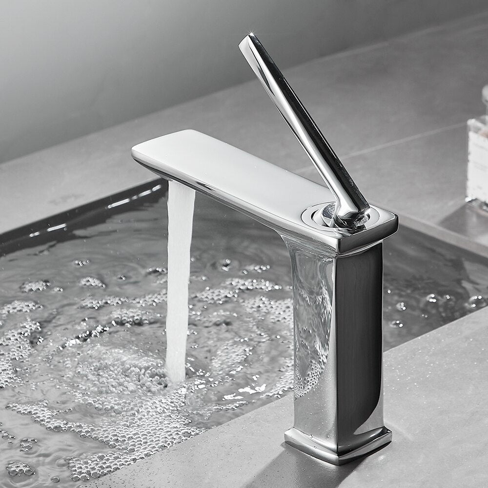 The Wasser™ Solid Brass Bathroom Faucet by Wanfan, featuring a modern chrome finish and sleek design, is turned on, releasing a stream of water into a stainless steel sink, creating bubbles and ripples.