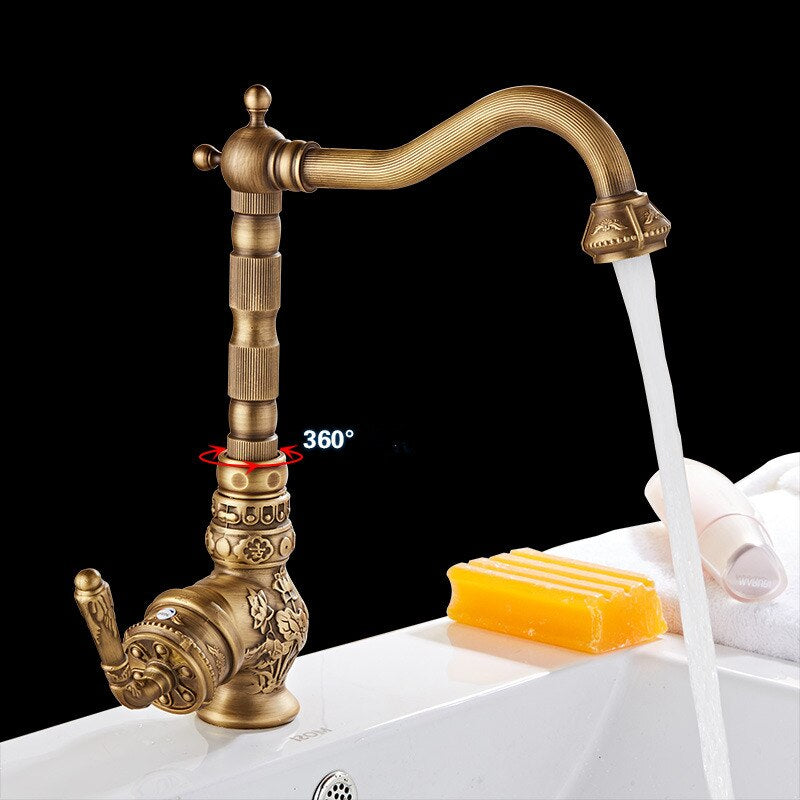 A Miho Single Handle Antique Bronze Faucet with intricate vintage-style designs is mounted on a marble countertop. The background features a beige marble-patterned wall, and a yellow soap bar is placed next to the faucet.