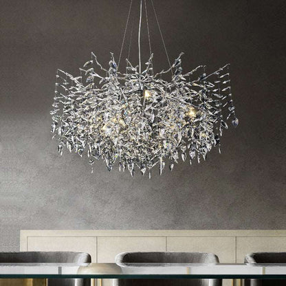 An Albero Collection Crystal Ceiling Light Fixture by Morsale.com, with intricate crystal detailing, hangs from the ceiling above a dining table with grey upholstered chairs. Emitting a soft, warm light from dimmable LED bulbs, the chandelier casts a cozy ambiance against a textured, dark wall in the background.