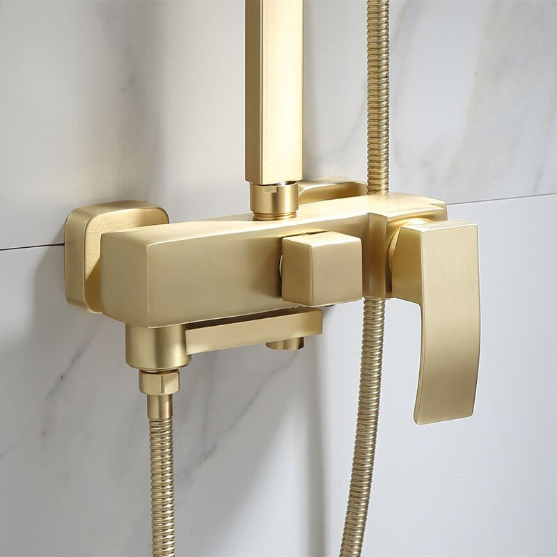 A modern bathroom featuring the Wasser™ Brushed Gold Shower System from Morsale.com, which includes a square overhead rain showerhead and a matching handheld showerhead. A detailed inset highlights the sleek gold faucet and lever controls of the stylish bathroom sink faucet. The background shows marble-style wall tiles and a hanging towel.