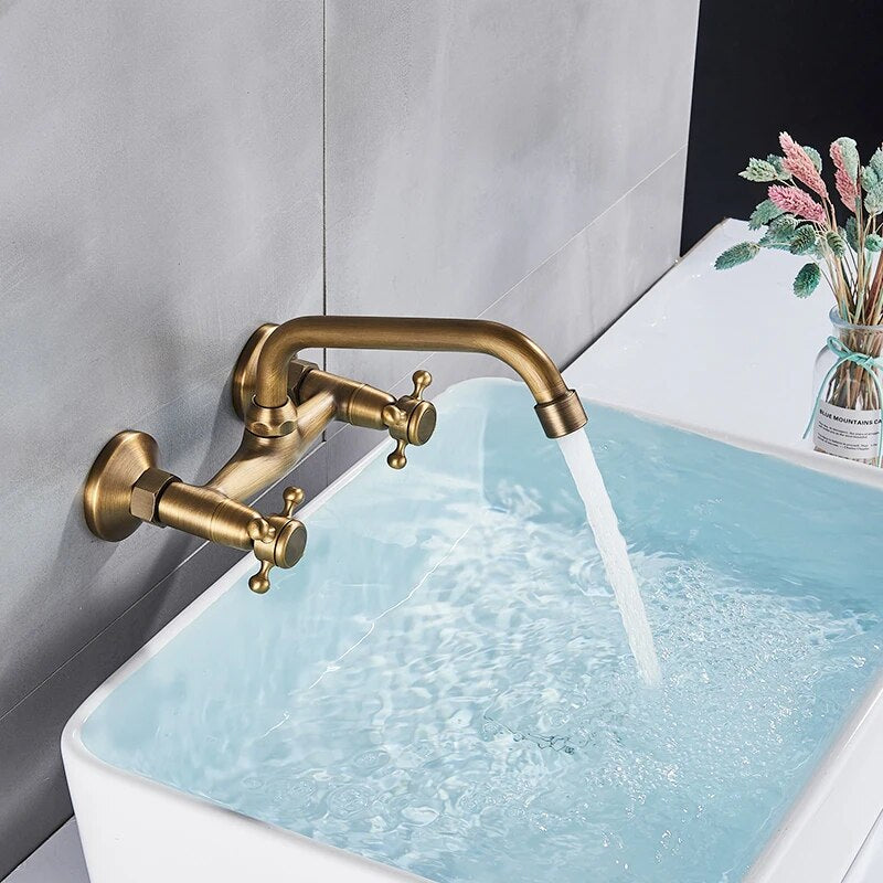 A Rozin Antique Brass Wall Mounted Bathroom Faucet with a vintage design is turned on, with water flowing into a sink or bathtub. These bathroom faucets feature two cross handles for hot and cold water, and the overall appearance gives a classic, antique feel.