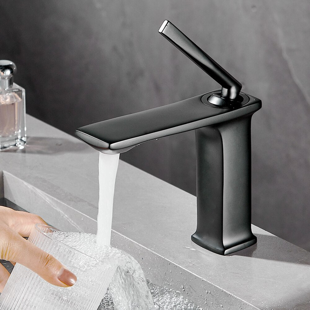 The Wasser™ Solid Brass Bathroom Faucet by Wanfan, featuring a modern chrome finish and sleek design, is turned on, releasing a stream of water into a stainless steel sink, creating bubbles and ripples.