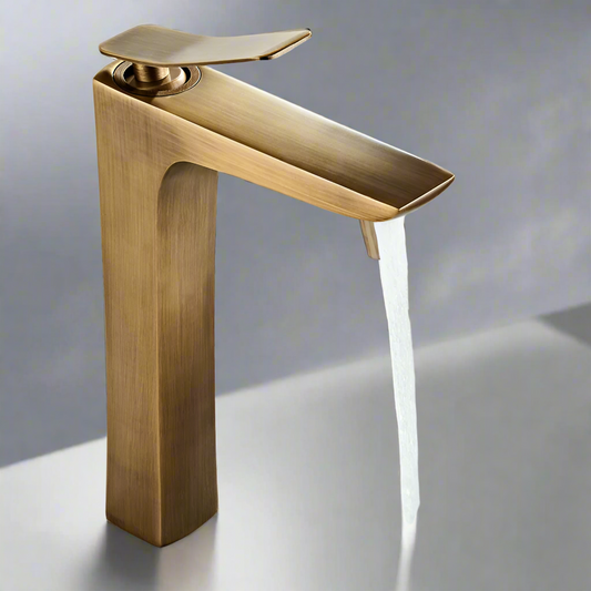 The Tiqui Antique Brass Deck Mounted Bathroom Sink Faucet features a modern, angular design and pours a steady stream of water into a glossy sink, all set against a neutral background.