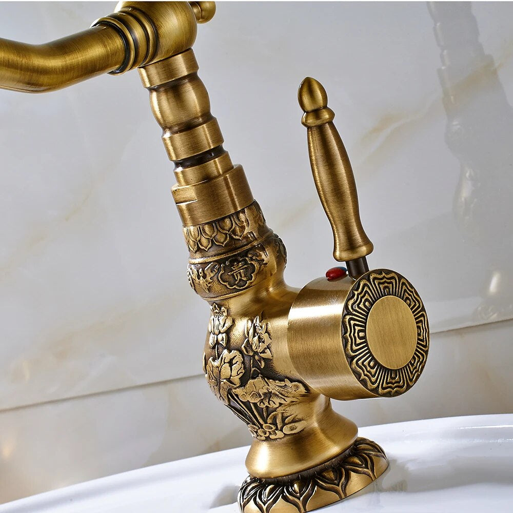 An Antique Brass Single Handle Faucet by Rozin, with its intricate carvings, streams water into a modern stainless steel sink against a textured white tile backsplash.