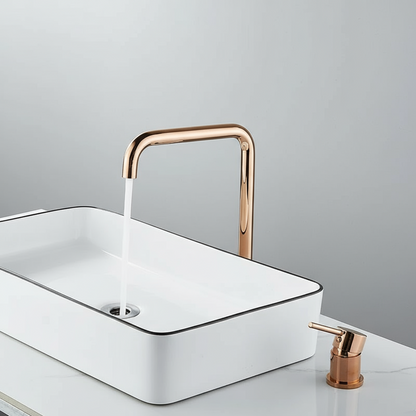 A modern bathroom sink features a white rectangular basin, an AllFixture Valmont Rose Gold Bathroom Sink Faucet with running water, and a matching rose gold soap dispenser on a sleek white countertop.