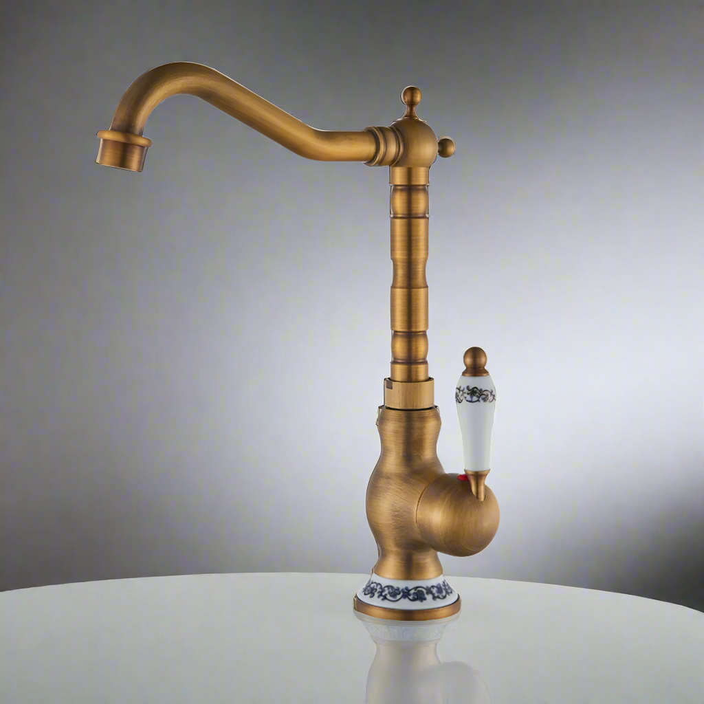 The Ellen Single Handle Antique Brass Kitchen Faucet features a vintage style with a high curved spout and a white porcelain handle with blue floral accents, crafted from solid brass in an antique bronze finish.