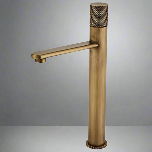 The Tiqui Antique Brass Bathroom Faucet features a modern cylindrical design with a side handle and matte brushed finish, showcased against a plain gray background.