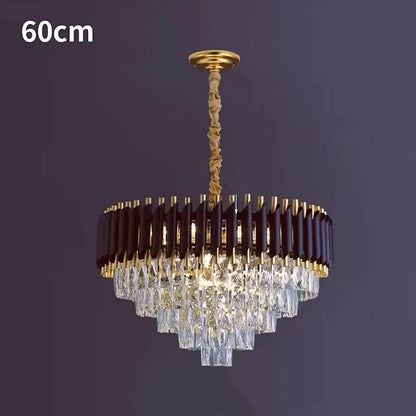 The Verano Crystal Chandelier by Morsale.com is a contemporary decorative lighting fixture featuring a 60cm diameter. Its chic sophistication is highlighted through a circular arrangement adorned with dark brown and gold accents. Multiple tiers of clear crystal prisms hang in an elegant pyramid shape, enhancing its luxurious appearance when set against a dark background.