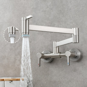 A modern gold Tiqui Wall Mounted Foldable Kitchen Pot Filler Faucet extends from a gray backsplash. The faucet, resembling a bathroom sink faucet, has a sleek, angular design with two adjustable arms for flexibility. It features two handles for hot and cold water and is shown with water streaming down. An aerator attachment is highlighted.