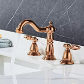 A Tiqui™ Solid Brass Contemporary Bathroom Sink Faucet, featuring a curved spout and two matching handles, is elegantly installed on a white marble countertop with a gray marble backsplash. Water flows from the faucet into the white sink below. A blue towel is partially visible on the left side.