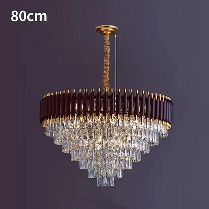 The Verano Crystal Chandelier from Morsale.com, boasting an 80cm diameter, elegantly hangs from the ceiling. It features a concentric brown and gold frame adorned with cascading rows of high-quality crystal-like rectangular prisms, creating sophisticated decor against a dark background.