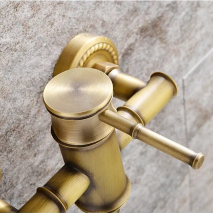 Ellen's Wasser™ Antique Brass Shower Faucet with Bathtub Faucet is mounted on a textured stone wall. The setup features a shower faucet with a lever handle, a diverter for switching water flow, and a detachable handheld showerhead with a flexible hose. Water is flowing from the faucet.