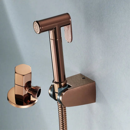 A sleek Tiqui Solid Brass Hand Held Bidet Sprayer mounted on a wall, exuding the elegance of high-end bathroom faucets. The sprayer features a hose connected to a wall bracket, and to the left, there is a bronze hose connector with a hexagonal handle against a light blue textured wall.