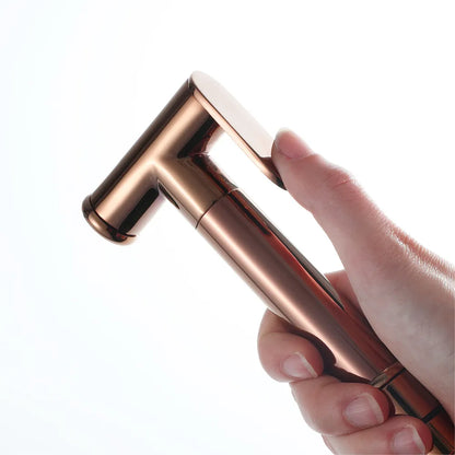 A sleek Tiqui Solid Brass Hand Held Bidet Sprayer mounted on a wall, exuding the elegance of high-end bathroom faucets. The sprayer features a hose connected to a wall bracket, and to the left, there is a bronze hose connector with a hexagonal handle against a light blue textured wall.