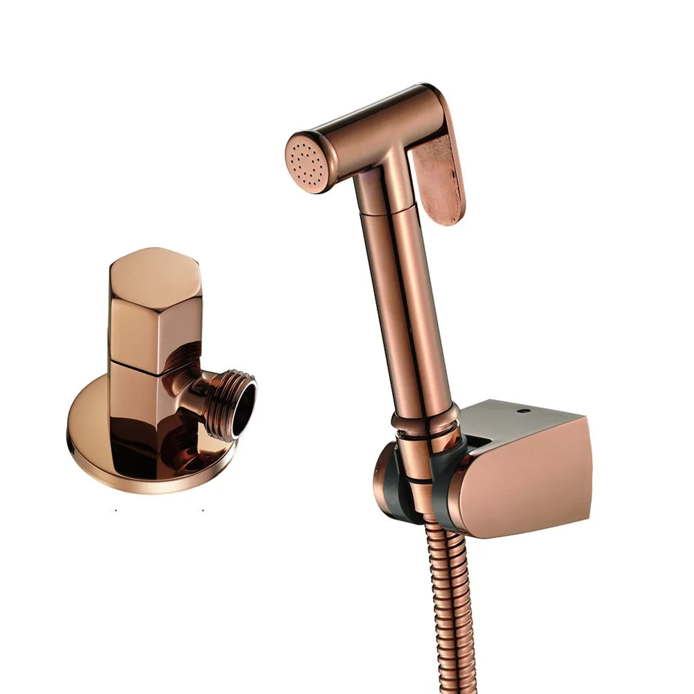 A sleek Tiqui Solid Brass Hand Held Bidet Sprayer mounted on a wall, exuding the elegance of high-end bathroom faucets. The sprayer features a hose connected to a wall bracket, and to the left, there is a bronze hose connector with a hexagonal handle against a light blue textured wall.