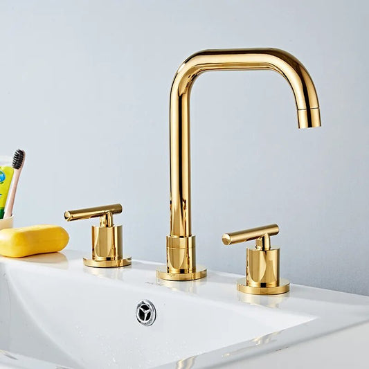 A modern bathroom features the Tiqui Windsor Widespread Bathroom Faucet with two matching brushed gold handles; in the background, a yellow toothbrush holder with a toothbrush is visible.