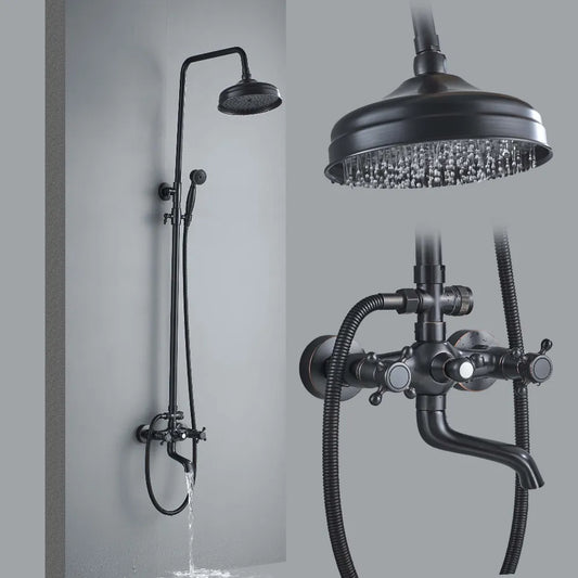 The Rozin Antique Bronze Complete Shower Faucet System Set features an overhead rain showerhead, a hand shower attachment, and a faucet. The image showcases a close-up of the round rain showerhead with water spraying and includes a detailed view of the faucet and knob controls, characteristic of high-end bathroom fixtures.