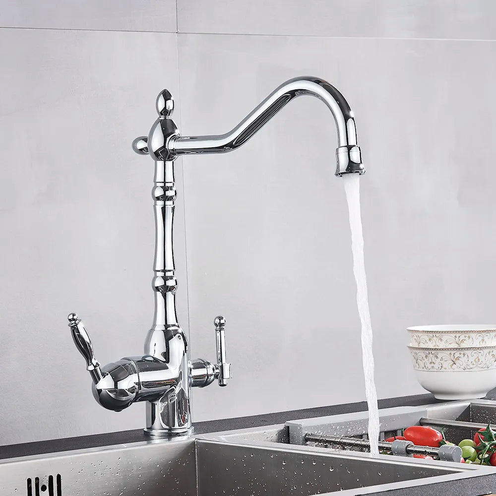 A modern Uythner chrome kitchen faucet with a filtered water tap releases a steady stream of water into a stainless steel sink filled with various vegetables. A ceramic bowl with an intricate pattern sits on the countertop, and the background is a minimalist gray wall.