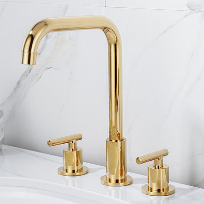 A Double Handle Solid Brass Deck Mounted Bathroom Faucet by Tiqui in a shiny gold finish stands out against a white marble backsplash. The faucet features a high-arched spout with two matching gold handles on either side, all elegantly positioned on a white countertop to create a modern and sophisticated design.