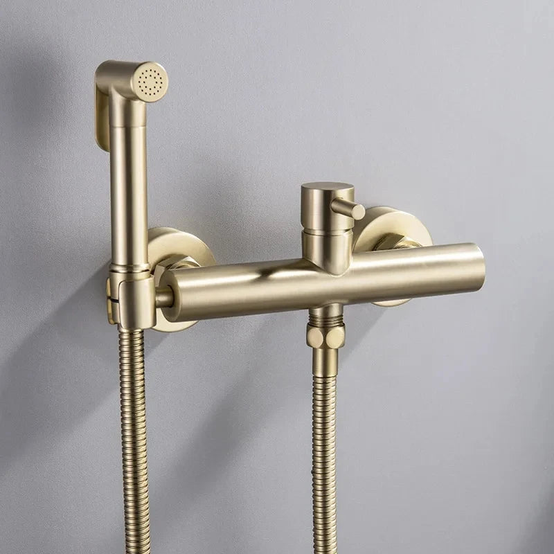 The Tiqui Cold And Hot Water Wall Mounted Bidet Faucet, featuring a sleek, gold-toned finish with a cylindrical control handle and flexible hose, boasts a minimalist yet contemporary design. This modern fixture, reminiscent of premium bathroom faucets, is mounted on a gray wall for an elegant look.