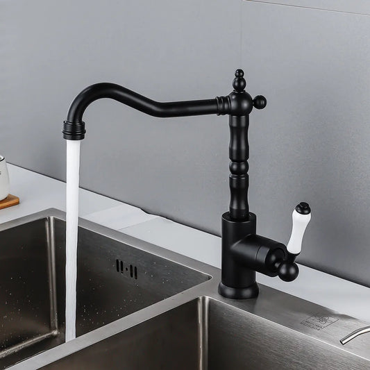 An Allfixture Single Handle Vintage Kitchen Sink Faucet in black, featuring a deck-mounted design and a white handle, is installed over a stainless steel sink. The faucet is turned on, releasing a steady stream of water into the sink. The background showcases a gray backsplash.