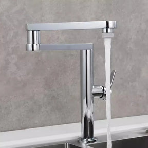 An Allfixture Deck Mounted Kitchen Faucet with Foldable Pot Filler is installed on a white counter. This modern faucet features a brushed gold finish, a single lever handle, and a tall, rectangular spout design with water flowing into the sink below. The background includes a light gray wall and part of another sink.