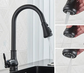 A Rozin Matte Black Pull-Down Kitchen Faucet with a high arc neck and single lever handle is seen in action, streaming water into a stainless steel sink. In the background, there is a leafy green vegetable and a cutting board on the countertop. The backsplash features a geometric design reminiscent of modern shower head patterns.