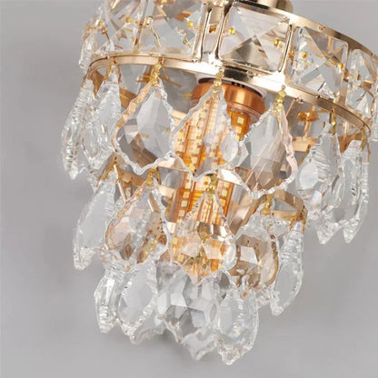 A close-up of an elegant Lazzo Kitchen Table Pendant Light Fixture. The chandelier, from Morsale.com, showcasing handmade crystals, features multiple hanging prisms arranged in tiers around a gold-colored frame, reflecting light with a warm, luxurious glow.