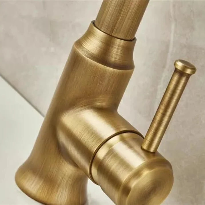 An Antique Brass Pull-Down Spout Kitchen Faucet by Rozin with a high arc and sleek, modern design pours water into a stainless-steel sink. The faucet handle is positioned to the right. In the background, reminiscent of elegant bathroom faucets, two white canisters with wooden lids are on a marble countertop.