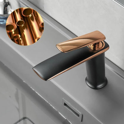 A sleek, modern Becola™ Brass Bathroom Faucet with a black and bronze finish is installed on a gray countertop. The faucet, branded by Becola, features a single lever handle with water flowing from the spout. The background showcases a light-colored, textured wall.