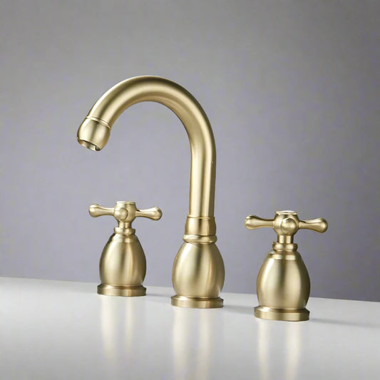 An Allfixture Widespread Dual Handle Bathroom Sink Faucet in brushed gold is mounted on a white countertop before a dark gray stone wall, with a glass perfume bottle placed to the left of the stylish fixture.
