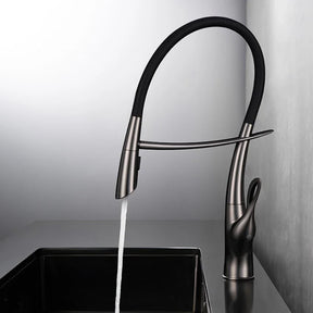 A Tiqui Single Handle Pull-Out Kitchen Faucet with a sleek, curved design is installed over a square, black sink. Water is flowing from the faucet, and the background features a minimalist setting with light-colored walls and a dark countertop.