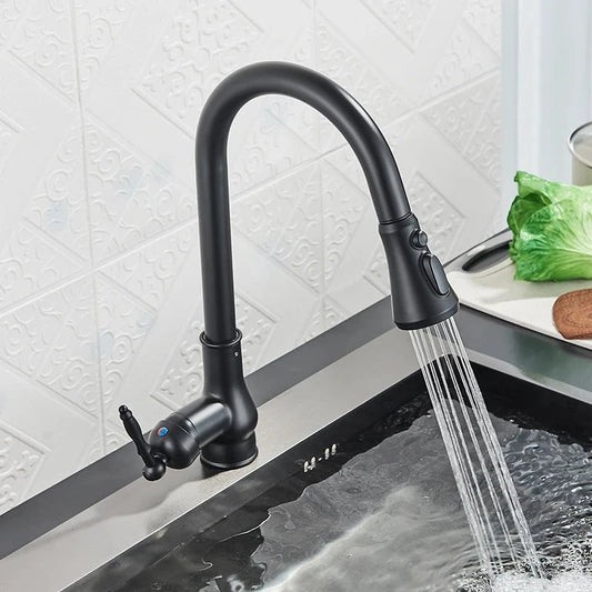 A Rozin Matte Black Pull-Down Kitchen Faucet with a high arc neck and single lever handle is seen in action, streaming water into a stainless steel sink. In the background, there is a leafy green vegetable and a cutting board on the countertop. The backsplash features a geometric design reminiscent of modern shower head patterns.