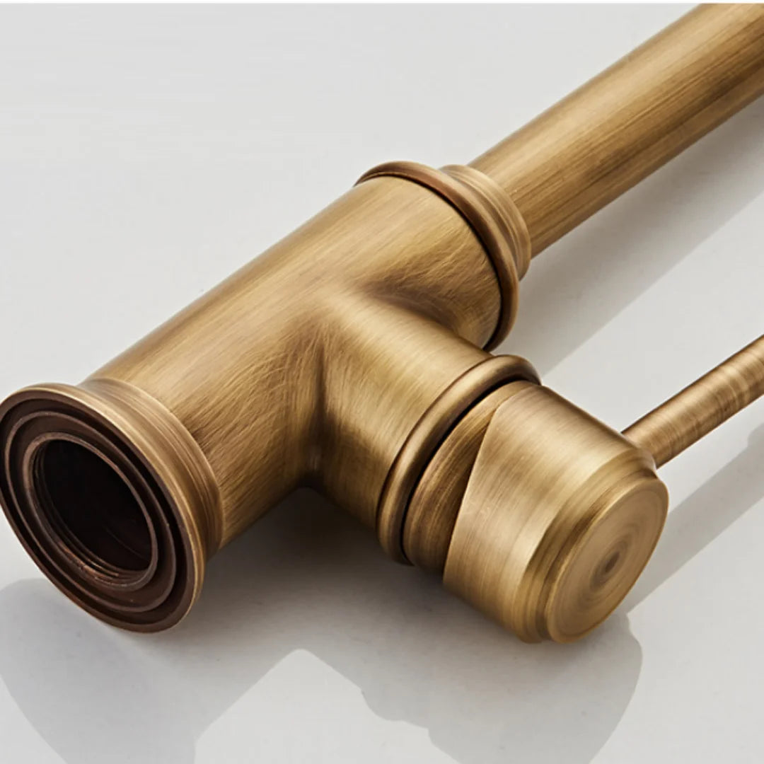 Close-up of AllFixture’s Maison Single Handle Bathroom Sink Faucet paired with a brass bottle trap pipe; both feature a brushed gold finish with cylindrical and T-shaped parts, shown against a plain, light background.