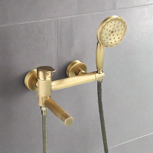 The Tiqui Antique Brass Handheld Shower Head With Bathtub Faucet is a modern, wall-mounted set installed against a textured, dark gray wall above a white bathtub. It features a handheld showerhead with water streaming out and a sleek bathtub faucet.