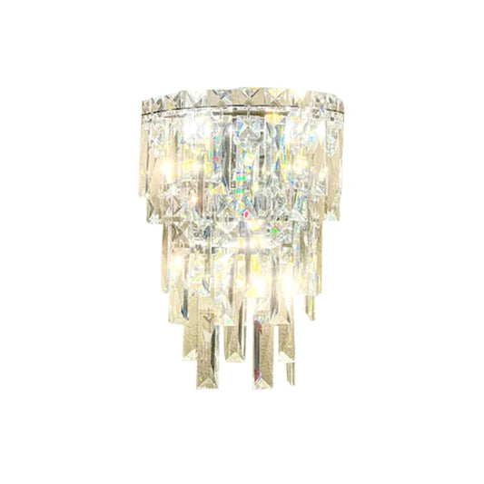 The Bacci Crystal Contemporary Wall Sconce by Morsale, featuring a sleek stainless steel finish and shining crystal prisms, complements a decorative chandelier gorgeously against a white background, adding contemporary lighting elegance.