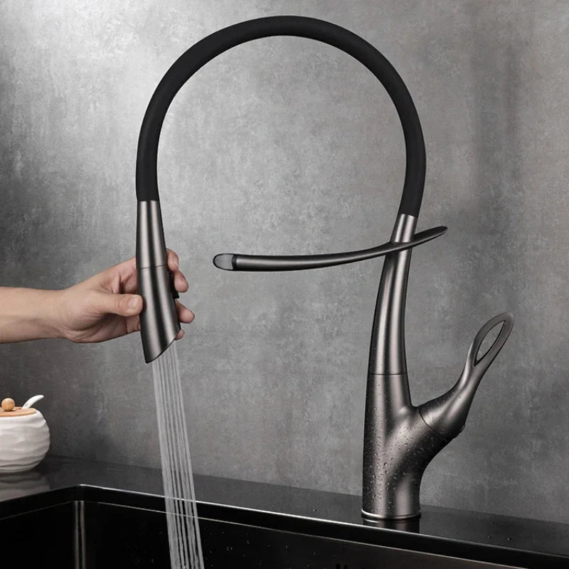 A Tiqui Single Handle Pull-Out Kitchen Faucet with a sleek, curved design is installed over a square, black sink. Water is flowing from the faucet, and the background features a minimalist setting with light-colored walls and a dark countertop.