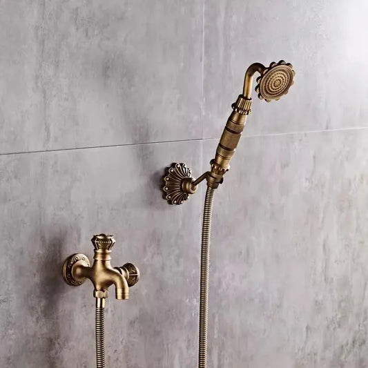 An Antique Brass Bidet Faucet by Allfixture, featuring an ornate handle and attached hose, is wall-mounted on a tiled surface. Below the bidet faucet is a matching valve with a decorative mount and intricate faucet, all in the same elegant brass finish.