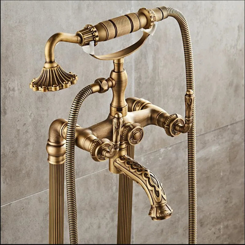 The Allfixture Antique Brass Floor Standing Bathtub Faucet Tub Filler boasts a vintage-style bronze design, featuring a handheld showerhead and dual control knobs. The luxurious fixture is mounted on a tiled wall, showcasing intricate details and an elegant finish reminiscent of antique brass.