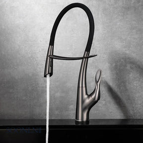 A Tiqui Single Handle Pull-Out Kitchen Faucet with a sleek, curved design is installed over a square, black sink. Water is flowing from the faucet, and the background features a minimalist setting with light-colored walls and a dark countertop.