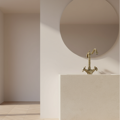 A minimalist bathroom features Allfixture’s Heritage Two Handle Bathroom Sink Faucet, paired with a beige sink and round mirror, all set against light walls and bright natural light.