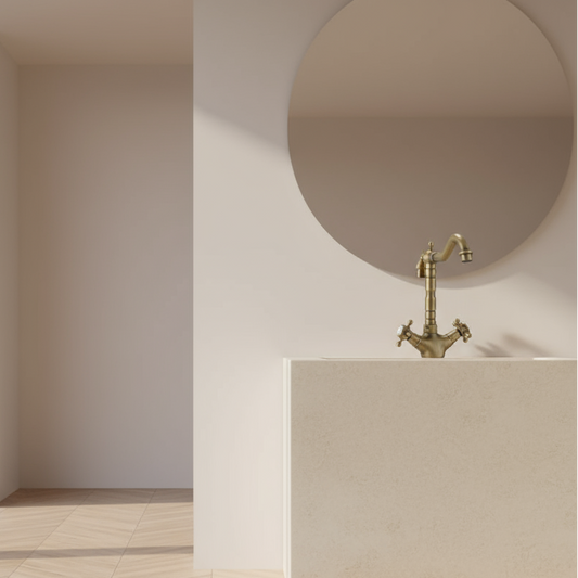 A minimalist bathroom features Allfixture’s Heritage Two Handle Bathroom Sink Faucet, paired with a beige sink and round mirror, all set against light walls and bright natural light.
