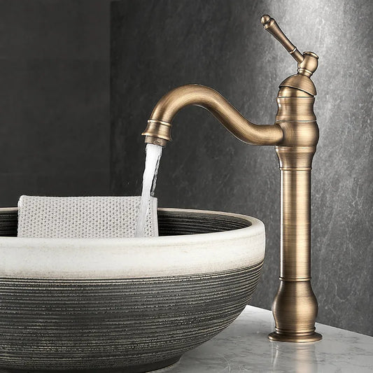 The Allfixture Heritage Bathroom Faucet in brushed antique brass pours water into a round stone vessel sink with a textured gray and white exterior, where a light-colored cloth rests beneath the stream.