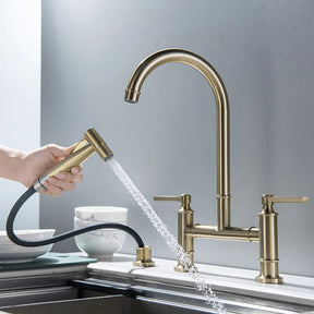 An Allfixture Brass Kitchen Faucet with Hand Sprayer is shown, featuring a high-arched spout and two handles for hot and cold water. A hand is using the detachable sprayer that is dispensing water into a sink, with ceramic mugs and a bowl in the background.