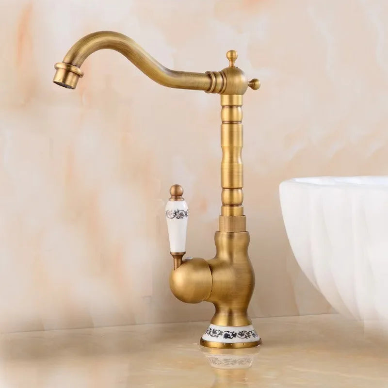 An Allfixture Tall Torneiras Bathroom Faucet – Single Handle, Hot and Cold Water Mixer, featuring a vintage-style brass finish with a white ceramic handle and decorative base, is installed next to a modern sink basin. Water flows from the faucet into the sink, set against a light beige background.