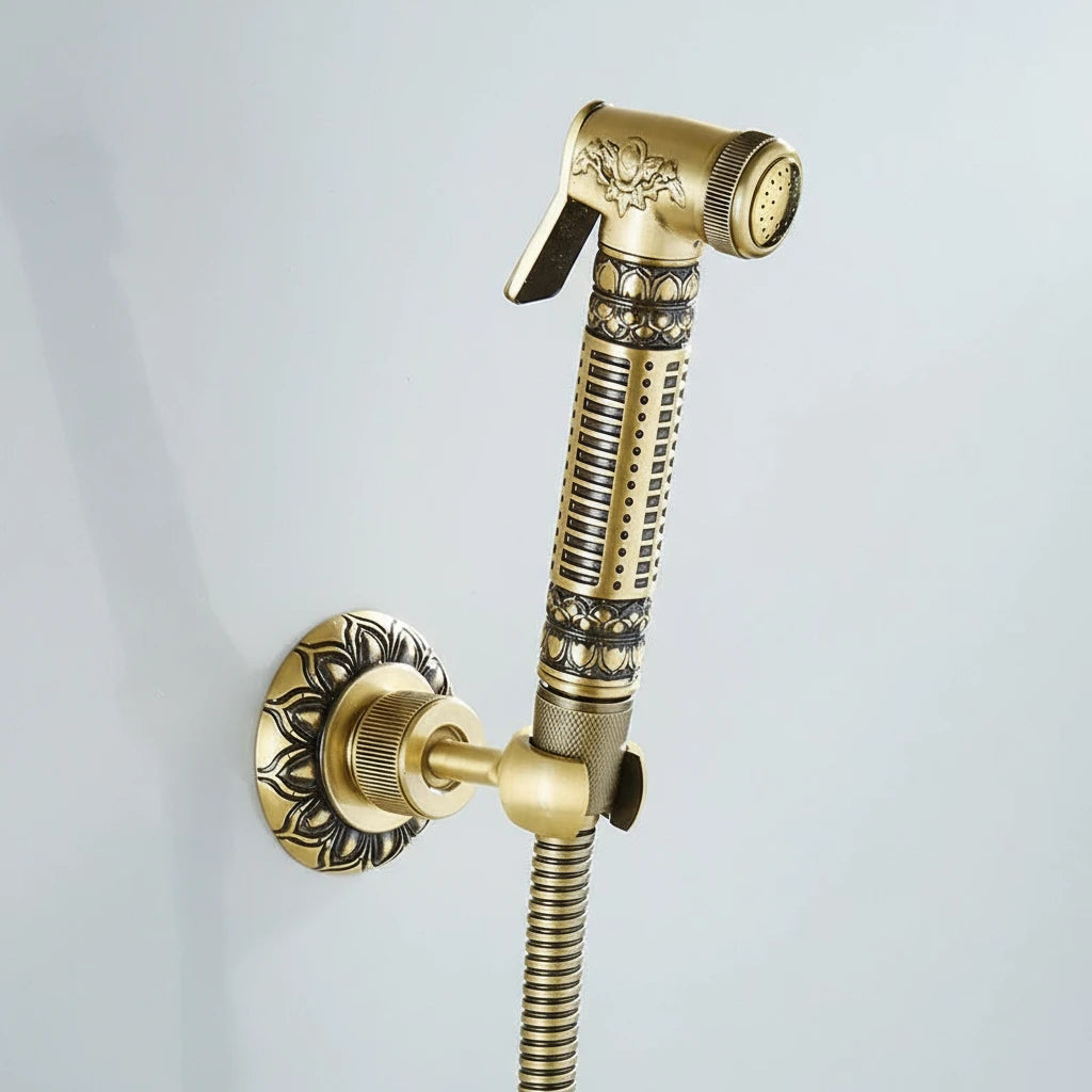 The AllFixture Heritage Toilet Sprayer & Bidet Faucet Set features a decorative, polished gold handheld sprayer with detailed floral and geometric patterns, mounted on the wall with a matching holder and hose.