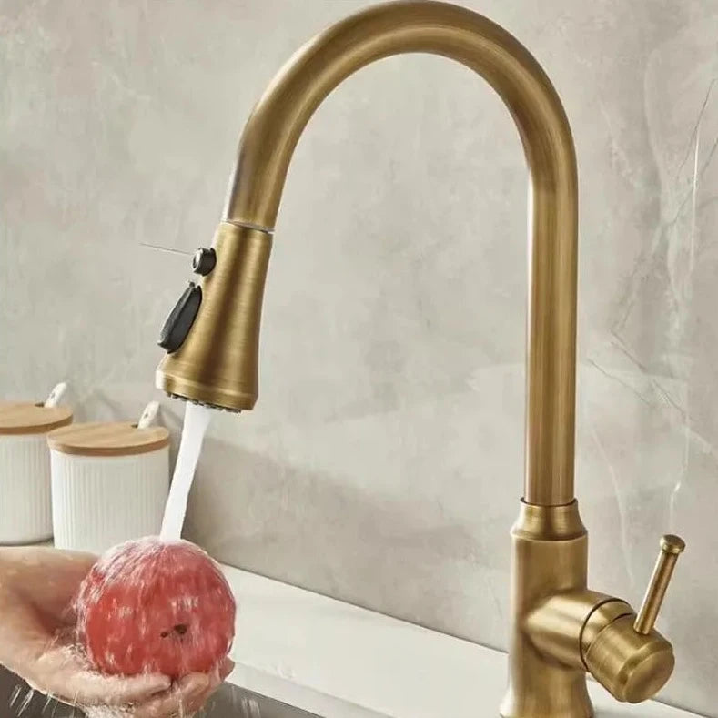 An Antique Brass Pull-Down Spout Kitchen Faucet by Rozin with a high arc and sleek, modern design pours water into a stainless-steel sink. The faucet handle is positioned to the right. In the background, reminiscent of elegant bathroom faucets, two white canisters with wooden lids are on a marble countertop.